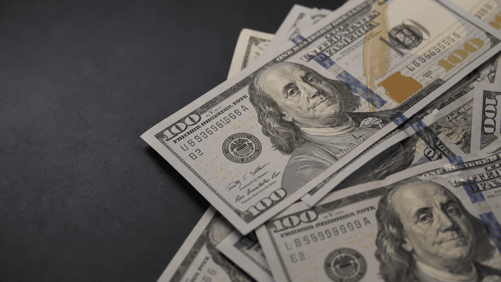 Overlapping U.S. 100-dollar banknotes on a dark surface
